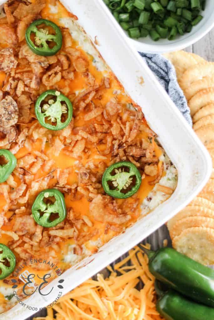 Top view of Jalapeno Popper Dip in a baking dish surrounded by ingredients and crackers on a table