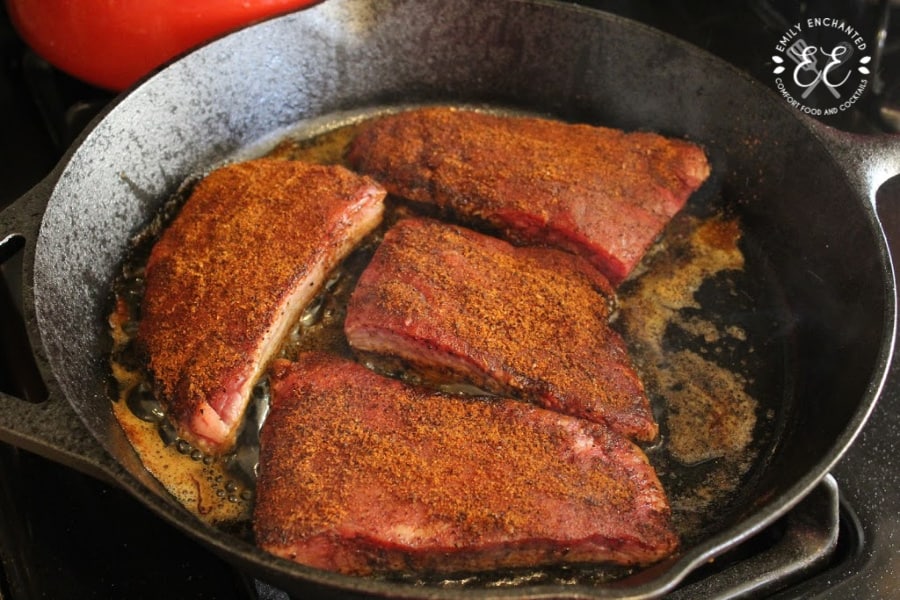 Seasoned flank steak searing in a cast iron skillet on a stove top