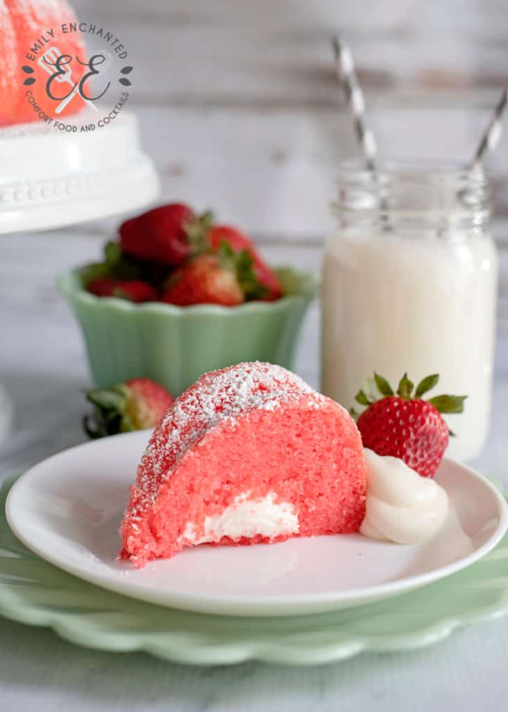 Slice of Strawberry Bundt Cake with Marshmallow Cream Filling on plate with glass of milk and bowl of strawberries in the background