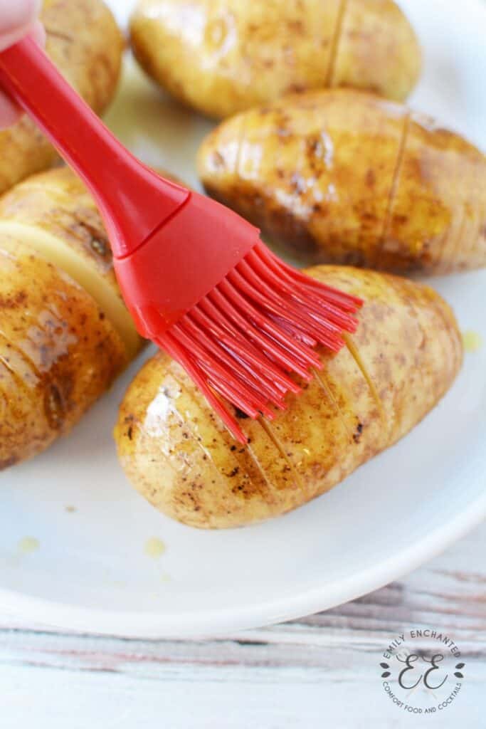 Russet potatoes being brushed with olive oil with a red brush