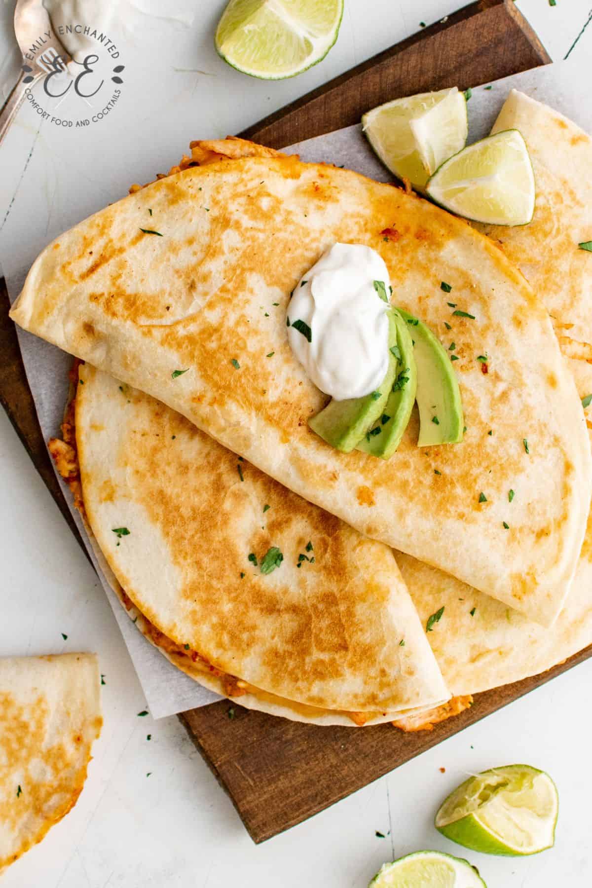 Chipotle Chicken Quesadillas on a cutting board with sour cream and avocado garnish