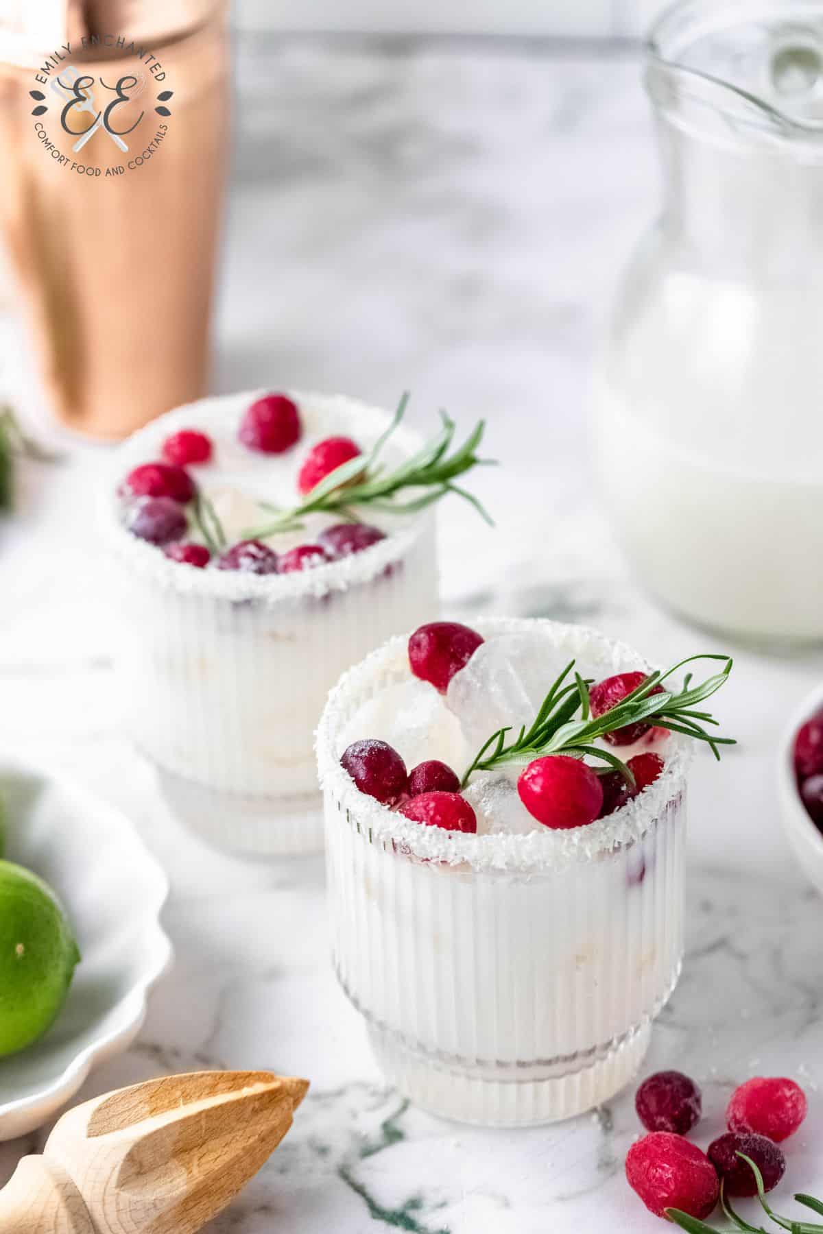 Two white christmas margaritas with garnish on a marble countertop