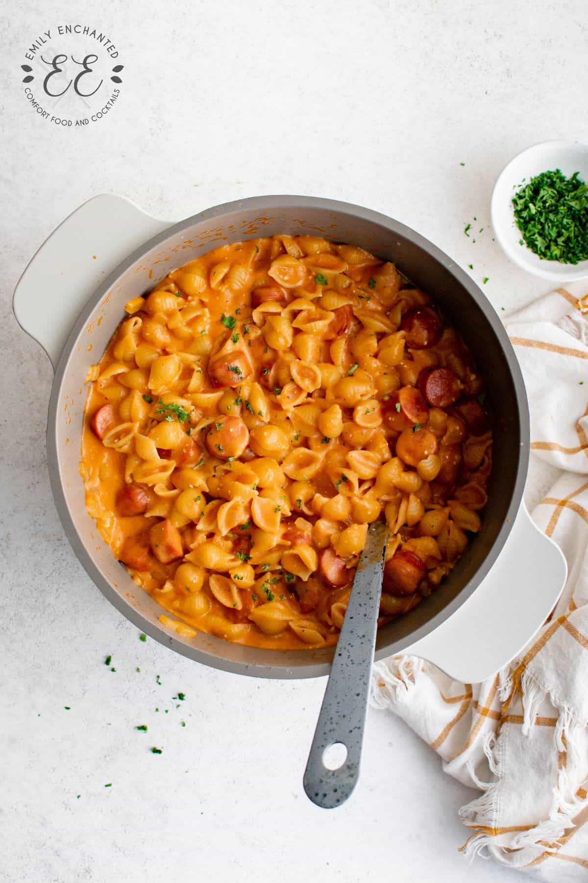 Hot Dog Pasta in a large pot with serving spoon and bowl of parsley ready to sprinkle